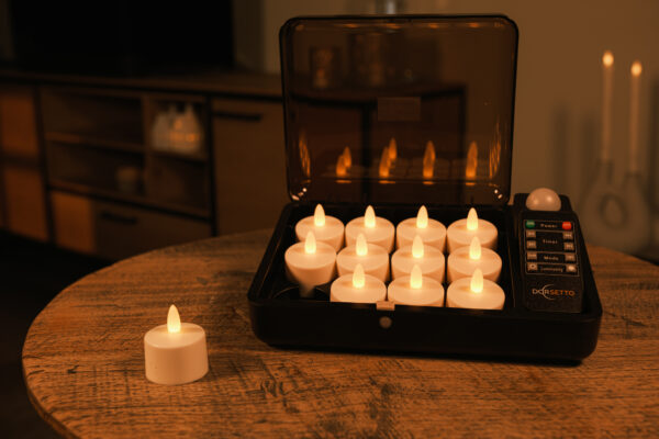 12 ładowalnych, wodoodpornych podgrzewaczy LED DORSETTO w czarnym etui ładującym na drewnianym stole – jeden podgrzewacz poza etui, w tle delikatnie oświetlony pokój