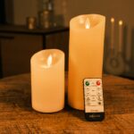 Dwie ładowalne świece LED z wosku DORSETTO o różnych wysokościach na drewnianym stole z pilotem – ciepłe światło i nastrojowe tło