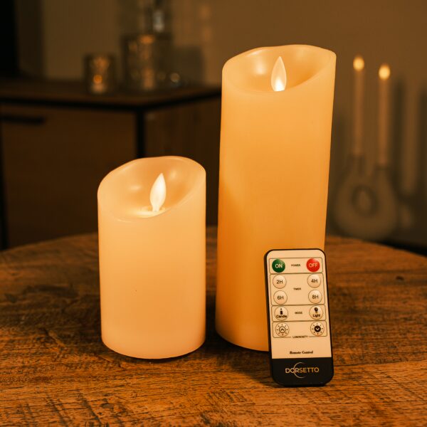 Dwie ładowalne świece LED z wosku DORSETTO o różnych wysokościach na drewnianym stole z pilotem – ciepłe światło i nastrojowe tło