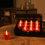 Dwanaście czerwonych ładowalnych LED tealightów DORSETTO ładowanych w czarnej walizce na drewnianym stole, sterowanych pilotem, tworzących ciepłą atmosferę w salonie.