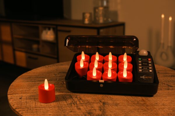 Dwanaście czerwonych ładowalnych LED tealightów DORSETTO ładowanych w czarnej walizce na drewnianym stole, sterowanych pilotem, tworzących ciepłą atmosferę w salonie.