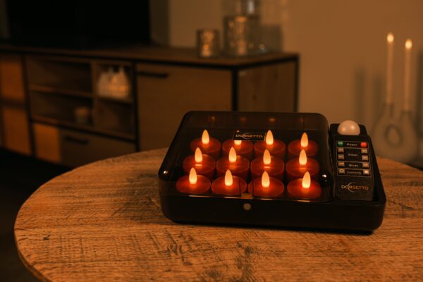 En sort ladestation med flere små, tændte LED-twistlys står på et træbord i et hyggeligt, svagt oplyst rum med dæmpet belysning og et træskab i baggrunden.