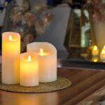 Świeca LED z wosku DORSETTO z ruchomym płomieniem na plecionej macie na drewnianym stole – nastrojowa aranżacja z dekoracyjnymi wazonami w tle