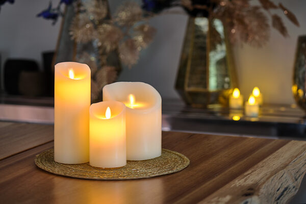 Świeca LED z wosku DORSETTO z ruchomym płomieniem na plecionej macie na drewnianym stole – nastrojowa aranżacja z dekoracyjnymi wazonami w tle