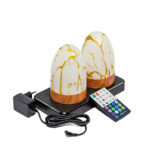 Zestaw dwóch ładowalnych, owalnych lamp stołowych DORSETTO z marmurowym, złotym wykończeniem na czarnej stacji ładującej. Obok znajduje się zasilacz i pilot. Lampy są wodoodporne i działają do 105 godzin.