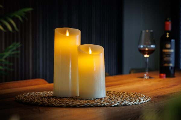 Zestaw 2 ładowalnych świec LED z wosku DORSETTO na plecionej podkładce, z kieliszkiem czerwonego wina i butelką w tle – przytulna, elegancka atmosfera