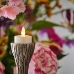 waxinelichtje met kaarsvet op houder op de achtergrond zijn roze bloemen te zien