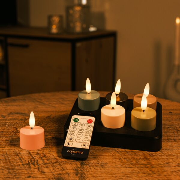 Sześć ładowalnych tealightów w różnych kolorach z pilotem zdalnego sterowania stoi na drewnianym stole, a tło jest nastrojowo rozmyte.