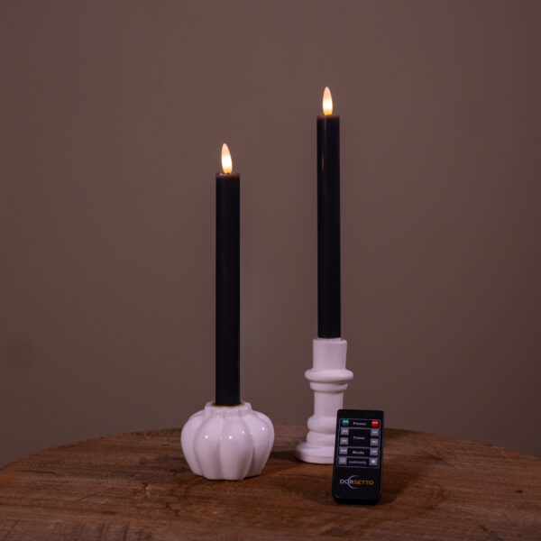 Dwie beżowe ładowalne świece stołowe LED (zestaw 2 szt., do 400 godzin świecenia) umieszczone w białych świecznikach – jednym w kształcie dyni, drugim cylindrycznym – stoją na drewnianej powierzchni, z pilotem z przodu, na jednolitym tle.