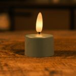 Mały LED tealight z ciepłym, żółtym płomieniem stojący na drewnianej powierzchni, tworzący przytulną atmosferę.
