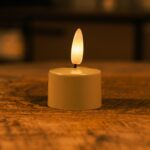 Niewielka LED świeca z ciepłym, delikatnie żarzącym się płomieniem stoi na drewnianej powierzchni, tworząc przytulną i nastrojową atmosferę.