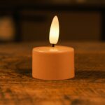 Niewielka świeca LED z ciepłym żółtym płomieniem stoi na drewnianej powierzchni, tworząc przytulną i nastrojową atmosferę.