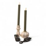 Dwie zielone świece w kremowych świecznikach, czarny pilot oraz czarny zasilacz stoją razem na białym tle. Świece wyglądają na elektryczne i mają końcówki w kształcie płomienia.Dwie zielone świece w kremowych świecznikach, czarny pilot oraz czarny zasilacz stoją razem na białym tle. Świece wyglądają na elektryczne i mają końcówki w kształcie płomienia.