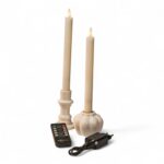 Dwie kremowobiałe stożkowe świece LED w białych świecznikach, z czarnym pilotem i zasilaczem, na białym tle. Realistyczny efekt płomienia.