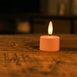 Zestaw 12 różowych ładowalnych podgrzewaczy LED z miękkim, żółtym płomieniem LED i pilotem stoi na drewnianym stole. Każdy podgrzewacz świeci do 400 godzin i tworzy nastrojowe oświetlenie w domu.