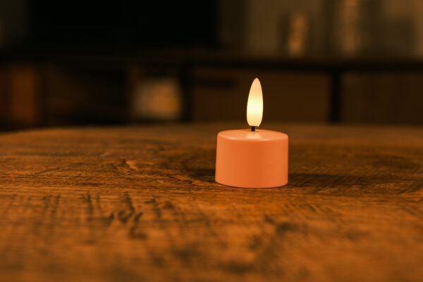 Zestaw 12 różowych ładowalnych podgrzewaczy LED z miękkim, żółtym płomieniem LED i pilotem stoi na drewnianym stole. Każdy podgrzewacz świeci do 400 godzin i tworzy nastrojowe oświetlenie w domu.