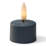 Mały, okrągły, ciemny LED tealight z plastikowym płomieniowym zakończeniem, zapalony tak, aby przypominał prawdziwą świecę, na białym tle.
