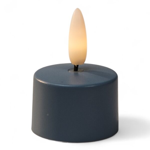 Mały, okrągły, ciemny LED tealight z plastikowym płomieniowym zakończeniem, zapalony tak, aby przypominał prawdziwą świecę, na białym tle.